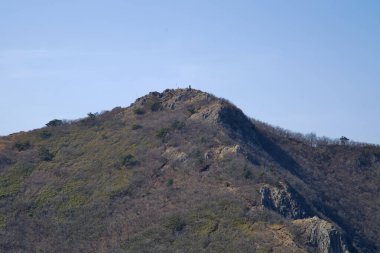 Ulsan Şehri, Güney Kore - 2 Nisan 2025: Gajisan 'ın kayalık zirvesi açıkça gökyüzüne karşı duruyor, bir taş işaretiyle işaretlenmiş ve Yeongnam Alplerinin tepesinde seyrek bahar bitkileriyle çevrili..