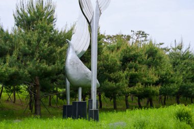 Incheon, Güney Kore - 19 Mayıs 2025: Soyut bir kuş heykeli Ara Waterway boyunca uzanan heykel parkındaki çam ağaçları ve bahar otları arasında yükselir ve modern biçimi doğal çevreyle harmanlar..