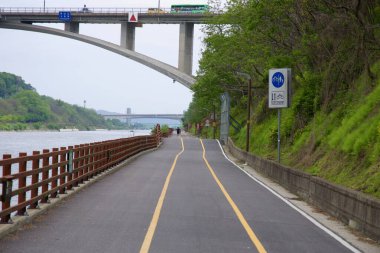 Incheon, Güney Kore - 19 Mayıs 2025: Bisikletçiler, Moksang Köprüsü 'nün altındaki Ara Bisiklet Yolu' nu belirlenmiş işaret ve çitle Gyeongin Ara Su Yolu boyunca yeşil kanal kenarındaki patikayı takip ediyorlar..