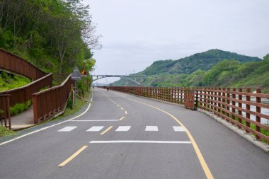 Incheon, Güney Kore - 19 Mayıs 2025: Ara Bisiklet Yolu, Gyeongin Ara Su Yolu 'nu takip ediyor, Moksang Köprüsü' ne doğru yavaşça kıvrılarak, yamaçtan geçen tahta bir yaya rampası ile.