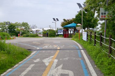 Incheon, Güney Kore - 19 Mayıs 2025: Bisikletçiler Ara Hangang Kilit Sertifika Merkezi 'ne açıkça belirtilmiş bir yol boyunca yaklaşıyorlar, Ara Kanalı ve Han Nehri arasındaki bu kavşakta güneş ışığı ve aynaların altından geçerek.