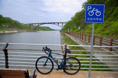 Incheon, Güney Kore - 19 Mayıs 2025: Ara Waterway Bisiklet Yolu üzerindeki bir dinlenme tesisinde, Moksang Köprüsü geniş kanal üzerinde kemerli bir yol bisikleti park edilmiştir..