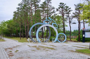 Incheon, Güney Kore - 19 Mayıs 2025: Bir bisikletçinin stilize tekerlek sürüşünün cesur bir heykeli Ara Bisiklet Yolu boyunca Ara Waterway yakınlarındaki sessiz bir çam korusuna uzanan Cheongna 'ya giden yolu işaret ediyor.