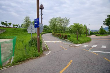 Incheon, Güney Kore - 19 Mayıs 2025: Duri Ekoloji Parkı yakınlarındaki Ara Bisiklet Yolu 'nda, ağaçların arasından park girişine uzanan ikincil bir patika ise bisikletçilere rehberlik ediyor..