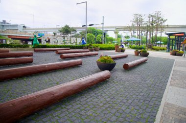 Incheon, Güney Kore - 19 Mayıs 2025: Ahşap oturma ve ekiciler Sicheon Waterside Parkı girişine yakın bir dinlenme alanı çiziyorlar..