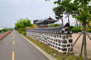 Incheon, Güney Kore - 19 Mayıs 2025: Suhyangwon pavyonu Ara Waterway bisiklet yoluna bakıyor, geleneksel taş duvarlar ve çam ağaçları geçen bisikletçiler için sessiz bir dinlenme yeri olarak gösteriliyor.