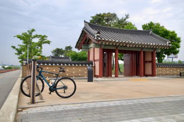 Incheon, Güney Kore - 19 Mayıs 2025: Joseon 'dan esinlenilen mimarinin nehir kenarındaki bisiklet yolu ile buluştuğu Ara Su Yolu boyunca Suhyangwon' un geleneksel kapısında bir bisikletçi dinleniyor.