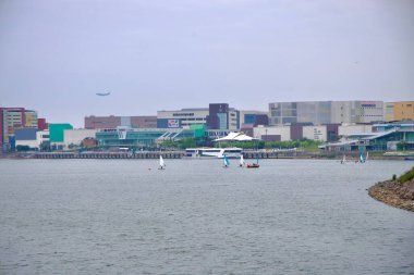 Incheon, Güney Kore - 19 Mayıs 2025: Ara Marina ve Ara Gimpo Yolcu Terminali 'nin yoğun lojistik merkezleri ve Gimpo Havalimanı yakınlarındaki alışveriş kompleksleri önünde yükselmesiyle Ara Waterway yakınlarında küçük yelkenliler yüzüyor.