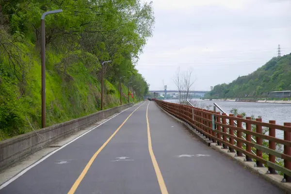 Incheon, Güney Kore - 19 Mayıs 2025: Ara Bisiklet Yolu Gyeongin Ara Su Yolu 'na paralel uzanır, yemyeşil bahar bitkisi ve ahşap bir çitle çevrili, uzak köprüler dumandan zar zor görülür..
