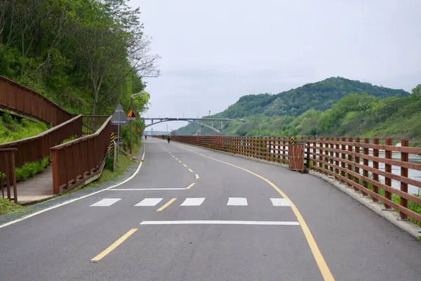 Incheon, Güney Kore - 19 Mayıs 2025: Ara Bisiklet Yolu, Gyeongin Ara Su Yolu 'nu takip ediyor, Moksang Köprüsü' ne doğru yavaşça kıvrılarak, yamaçtan geçen tahta bir yaya rampası ile.