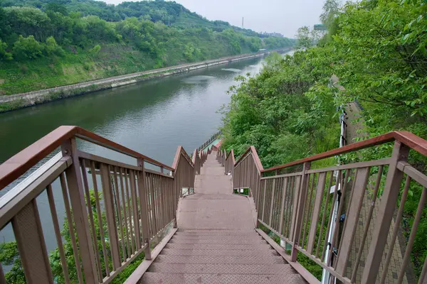 Incheon City, Güney Kore - 19 Mayıs 2025: Ara Şelalesi 'nden aşağıdaki Ara Kanalı bisiklet yoluna dik bir merdiven iniyor, ormanlık tepeler ve yaya yolları arasındaki su yolu manzarası sunuyor.