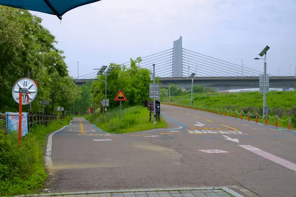 Incheon, Güney Kore - 19 Mayıs 2025: Ara Hangang Kilidi 'nden geri dönüşümlü iniş, arka planda Jeonho Köprüsü ve yol gösteren açık işaret ile Gangseo Hangang Parkı' na bisikletçileri götürüyor..
