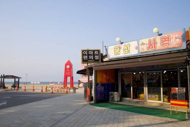 Donghae, Güney Kore - 1 Haziran 2025: Bir market ve balon avlama tezgahı Mangsang Sahili 'nde, yolların kumla buluştuğu ve Doğu Denizi' nin başladığı ikonik kırmızı saat kulesinin yanında oturur..