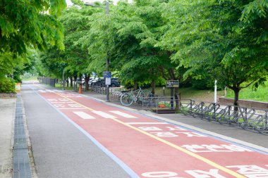 Namyangju, Güney Kore - 19 Mayıs 2025: Kırmızı işaretli bisiklet yolu, Hangang bisiklet yolu boyunca önemli bir durak olan Neungnae İstasyonu 'nun yanındaki gölgeli bisiklet parkının yanından geçiyor.