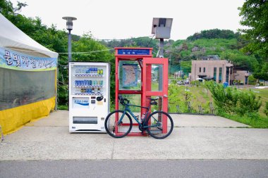 A vending machine, red phone booth with a certification stamp, and cyclists bike mark the Neungnae Station checkpoint on the Bukhangang Bicycle Path.