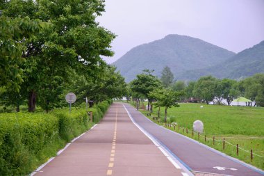 Namyangju Şehri, Güney Kore - 19 Mayıs 2025: Namyangju Su Bahçesi 'nden geçen özel bisiklet yolu, çevresi tarlalar, ağaçlar ve Bukhangang Nehri boyunca uzanan uzak dağlarla çevrili..