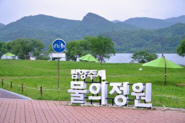 Namyangju Şehri, Güney Kore - 19 Mayıs 2025: Namyangju Su Bahçesi 'ne şemsiyeler ve nehir manzaralı büyük bir tabela, Bukhangang boyunca uzanan bu bereketli ekolojik parka ziyaretçileri karşılıyor.