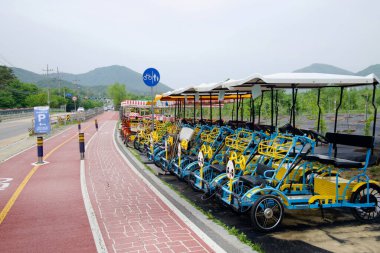 Namyangju Şehri, Güney Kore - 19 Mayıs 2025: Namyangju Su Bahçesi yakınlarındaki kırmızı bisiklet yolunda dört tekerli renkli bisiklet kuyrukları, Bukhangang boyunca aile dostu gezintiler sunuyor.
