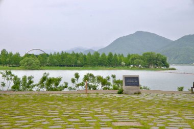 Namyangju City, South Korea - May 19th 2025: Looking across the North Han River from Balgeun Gwangjang toward Namyangju Water Garden, with Baetnari Bridge and forested hills forming a serene riverside backdrop.