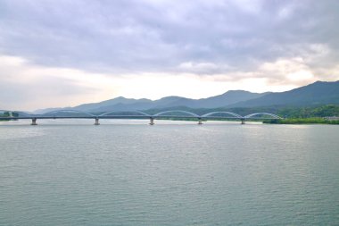 Yangpyeong County, South Korea - May 19th 2025: A wide view of Yangsu Bridge, its elegant arches stretching across the North Han River with mountain ridgelines layered beneath a moody sky.
