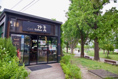 Yangpyeong County, South Korea - May 19th 2025: Cafe Garam, a modern black building with glass walls, sits beside a tree-lined path near the Han River at Dumulmeori, welcoming visitors with cozy seating.