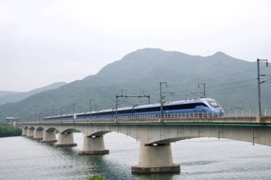 Tam teşekküllü bir GyeonguiJungang Hattı treni Yangsu Demiryolu Köprüsü boyunca uzanır. Kuzey Han Nehri üzerindeki orman dağları ve bulutlu gökyüzü tarafından çerçevelenir..