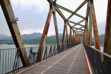 Yangpyeong İlçesi, Güney Kore - 19 Mayıs 2025 Bukhangang Demiryolu Köprüsü manzarası paslı çelik kirişleri ve nehir boyunca uzanan düz bir bisiklet yolunu ortaya çıkardı..