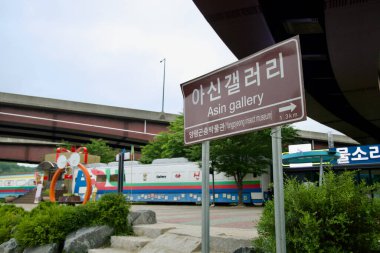 Yangpyeong İlçesi, Güney Kore - 19 Mayıs 2025: Kahverengi yol işareti Asin Galerisi 'ne 1,3 km uzaklıktaki Asin tren istasyonunun altında renkli bir tren-araba sanat müzesinin yanındaki üstgeçidin altında.