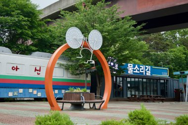 Yangpyeong İlçesi, Güney Kore - 19 Mayıs 2025: Bisiklet esinlenilmiş turuncu kemerli bir heykel, yeniden tasarlanmış Asin tren galerisi ve Mulsorigil binasının önündeki tezgahı çerçeveler..