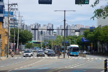 Busan 'da BEXCO yakınlarında, apartman kuleleri ve ışık bulutlarının altındaki kalabalık şehir koridoru tabelalarıyla birlikte geniş şeritler ve özel otobüs güzergahları boyunca trafik ilerliyor..