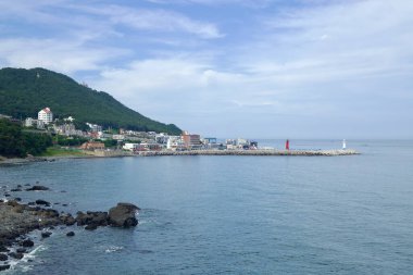 Cheongsapo limanındaki yaya köprüsünden girişi işaretleyen kırmızı ve beyaz deniz fenerleriyle ve arkadaki orman tepeleriyle bakıyorum..