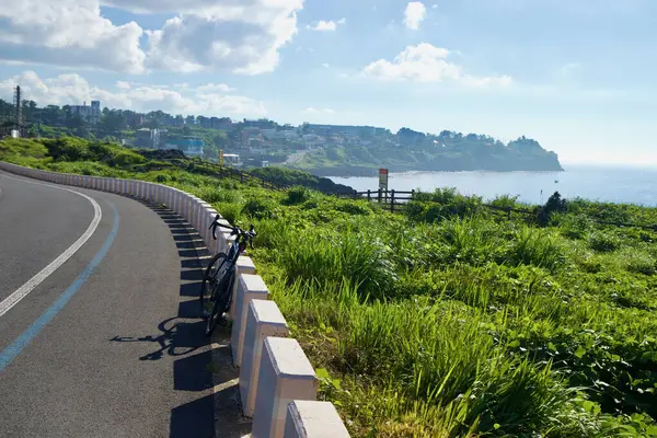 Bir yol bisikleti Hagu-Aewol Sahil Yolu boyunca alçak bloklara yaslanıyor, mavi benekli ve yeşil burunlu sahil kasabasına doğru koşuyor..
