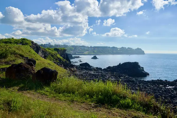 Lav kayalıkları ve tıkanmış kayalar Jeju şehrinin batısındaki sakin bir körfezin üzerindeki burnu sisli sabah ışığı altında karşı kıyıya uzanan sahil kasabasını oluşturur..
