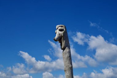 Jeju Adası 'ndaki Hanlim Limanı' nın kıyısındaki derin mavi gökyüzüne karşı yontulmuş ahşap bir totem yükseliyor. Yıpranmış tahılları ve düşük kıyı bulutlarının üzerinde duran stilize özellikleri..