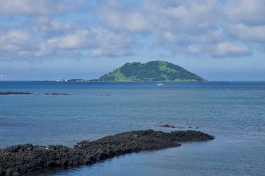 Koyu bazalt geçitleri ve resifler, pamuk bulutlarının altındaki Biyangdo Adası 'na doğru sığ mavi sulara doğru uzanır..