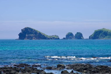 Açık deniz adaları mavi Doğu Çin Denizi boyunca bir hat oluşturarak bazalt kayalarda hafif dalgalar oluşturur. Sahne, Jeju 'nun batı kıyısındaki Chagwidos sahiline bakıyor..