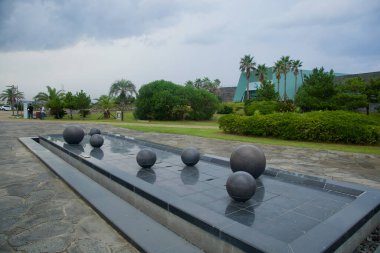 Seogwipo Şehri, Güney Kore - 7 Eylül 2025: Taş çeşmeleri, palmiye ve manikürlü çalılarla çevrili Jeju Gezegeni 'nin dışında sığ bir yansıtma havuzu nokta.