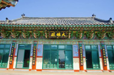 Daeungjeon salonu cephesinde zengin boyanmış dancheong kirişleri, hat panelleri ve yeşil pencere kafesleri yer alıyor ve Seongsan yakınlarındaki tapınağın resmi bir ön görüntüsünü sunuyor..