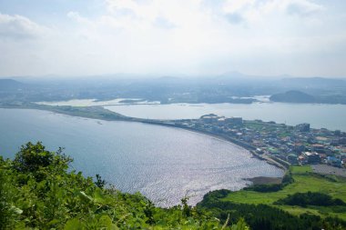 Güneş ışığı Seongsan Ilchulbong 'un altındaki körfez boyunca dalgalanır kıyı mahalleleri, sulak alanlar ve körfezler boyunca uzanan uzun geçitlerle uzak oreum' a doğru uzanır..