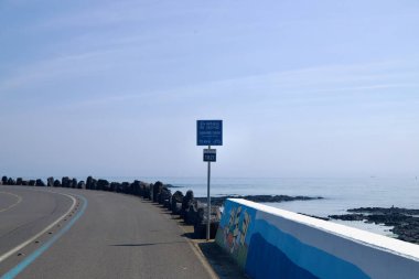 Jeju Fantezi Bisiklet Yolu 'ndaki bir işaret Gimnyeong Sahili' ne 10.4 kilometre olduğunu gösteriyor. Sahil duvarı ve siyah lav kıyısı sakin deniz boyunca uzanıyor..