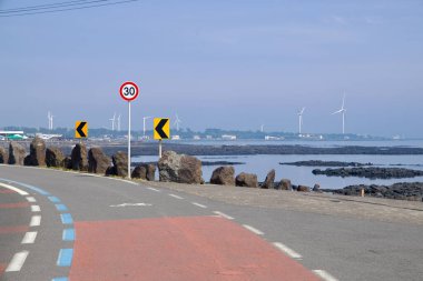 Handong-ri kıyısı, siyah lav resiflerinin durgun suyla buluştuğu gelgit düzlüklerinin etrafında bükülür. Ufuk boyunca dönen rüzgar türbinlerinin oluşturduğu bir çizgi vardır..