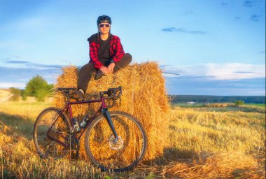 Bisikletçi gün batımında bisiklet sürdükten sonra samanlıkta oturur. Etkin yaşam tarzı ve seyahat kavramı.