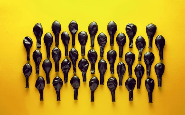 Black deflated balloons on yellow background.