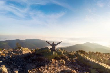 Dağın tepesinde kollarını kaldırmış gün batımında sisli güzel dağ vadisine bakan bir kız. Dağlardaki güzel sabah manzarası. Seyahat ve turizm.