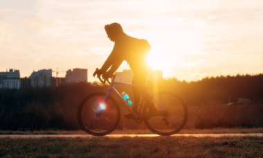 Dramatik bir günbatımı arka planında bisiklet süren bir bisikletçinin silueti. Yumuşak odak.