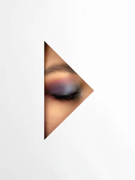 Beautiful woman\'s eye with colorful make-up through the triangle in white paper.