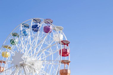 Mavi gökyüzünün arka planında çok renkli taksileri olan dönme dolap.