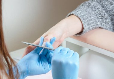 Mavi eldivenli manikürcü güzellik salonunda tırnak törpülüyor..
