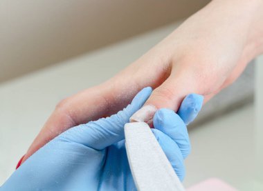 Mavi eldivenli manikürcü güzellik salonunda tırnak törpüsü takıyor..