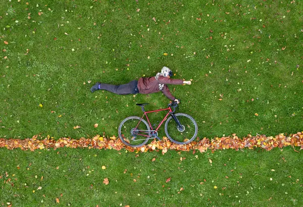Young lies on the green lawn in a superman pose with a bicycle. Creative trendy autumn concept. Drone top view.